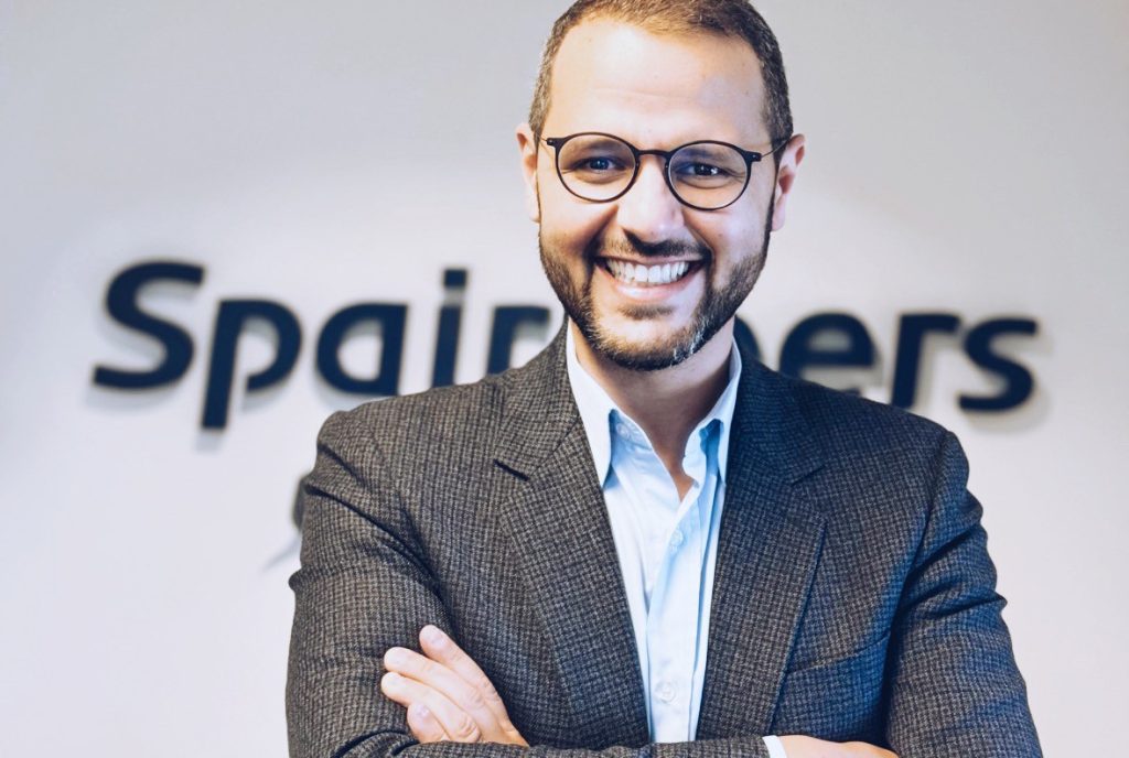 Portrait showing Abdelouahab El Fettouhi standing in front of white wall with logo sign of Spairliners.